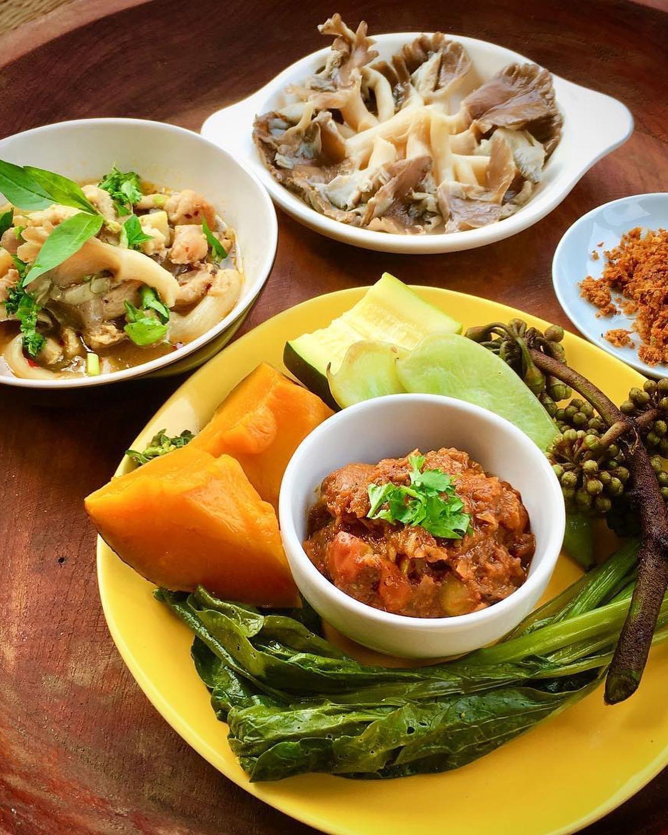 Thai food bowls of curry and fresh herbs on a rustic wooden table.